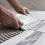 صورة فني تركيب سيراميك يعمل على حمام أبيض ورمادي