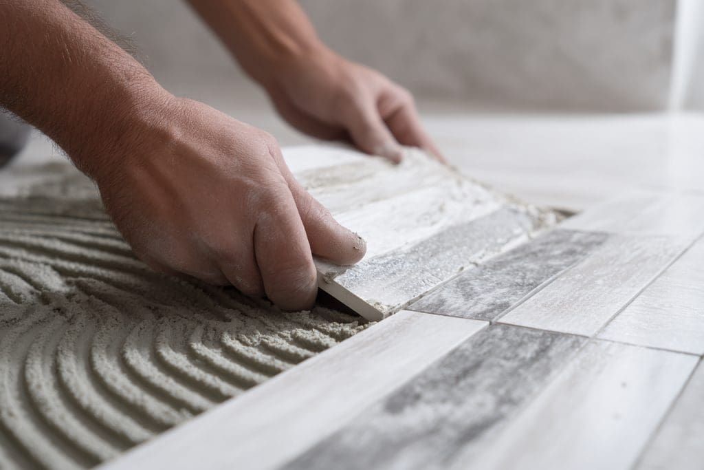 صورة فني تركيب سيراميك يعمل على حمام أبيض ورمادي